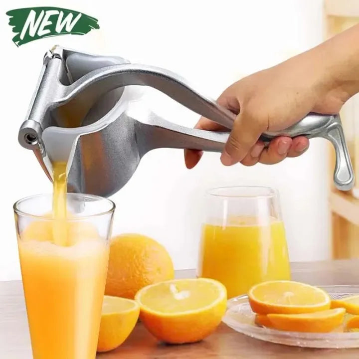 Hand pressing manual metal citrus juicer over glass with fresh orange juice and whole oranges